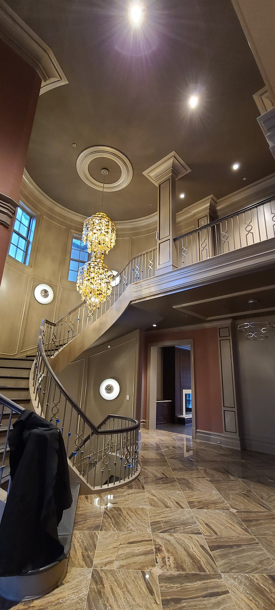 A grand curved staircase rising past crystal chandeliers and ornamental ceiling millwork