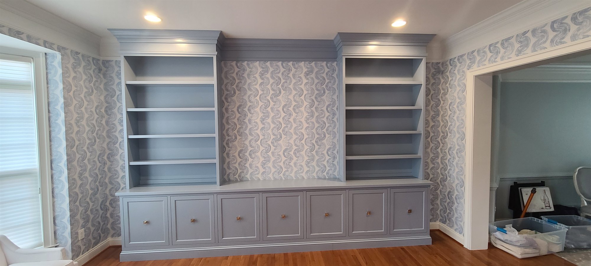 Twin painted bookcase built-ins flanking a media base against patterned wallpaper